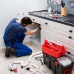 plumber-wearing-blue-overalls-replacing-kitchen-sink-drain-pipe-with-tools-next-to-him